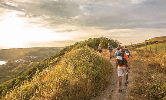 Walkers make their way along a path with grassy banks and a dramatic sunset Walkers make their way along a path with grassy banks and a dramatic sunset