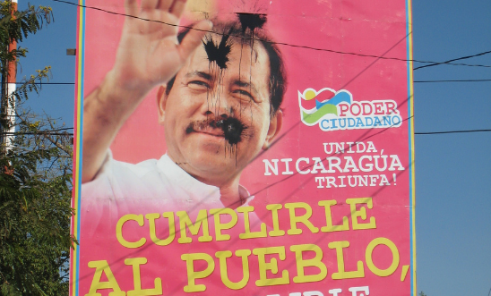 Paint-bombed government poster on a street in Managua.