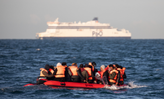 Migrants packed tightly onto a small inflatable boat bail water out as they attempt to cross the English Channel near the Dover Strait