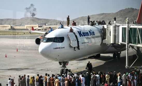 Afghan people climb on top of a plane as they wait at the Kabul airport in Kabul on August 16, 2021