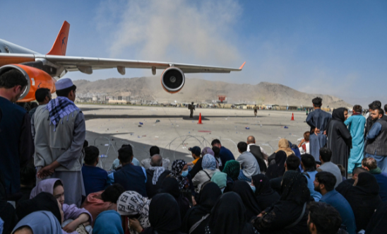 Afghan people sit as they wait to leave the Kabul airport in Kabul on August 16, 2021