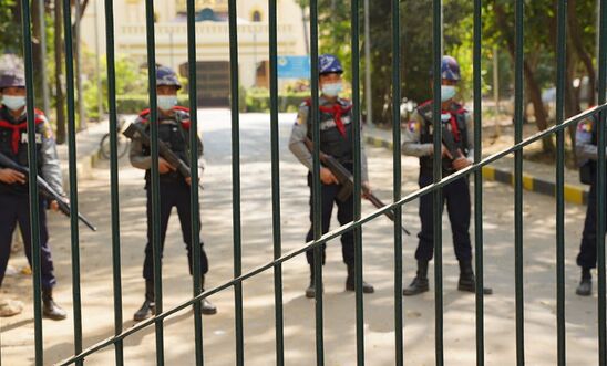Picture of five armed policemen standing in a line behind a gate during a protest in Myanmar in February