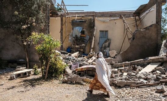 A woman walks in front of a war damaged house 