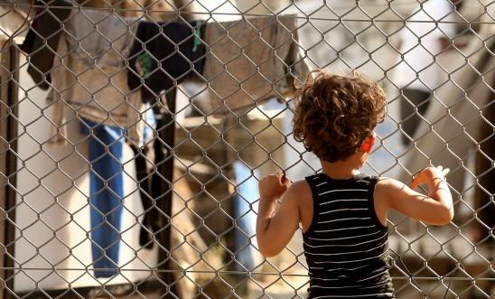 A refugee child looks through a fence at the Moria refugee camp on May 20, 2018 in Mytilene, Greece