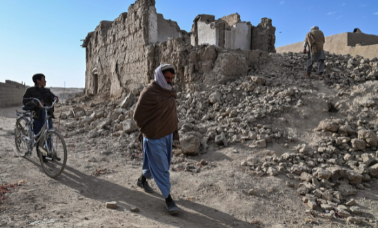 In this photograph taken on November 16, 2021, people walk past the ruins of destroyed houses in Arzo village on the outskirts of Ghazni