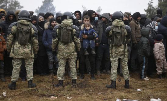Migrants stand in front of Belarusian servicemen as they gather in a camp near the Belarusian-Polish border in the Grodno region on November 14 2021 Migrants stand in front of Belarusian servicemen as they gather in a camp near the Belarusian-Polish border in the Grodno region on November 14 2021