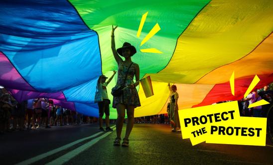 An image of a person under a rainbow flag while attending a protest for LGTBI+ rights