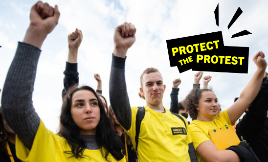 3 young people wearing Amnesty yellow shirts stand with their hands raised in fists