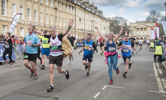 Image shows people running through bath with their arms raised and smiling.