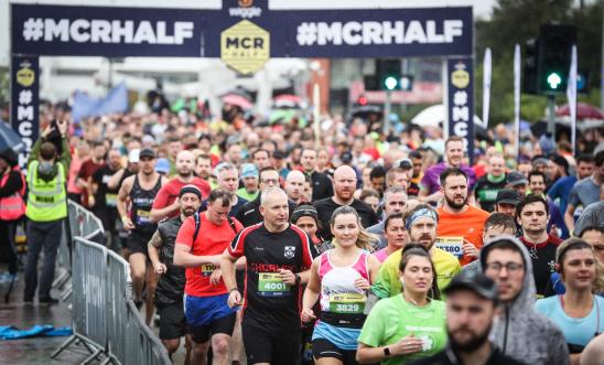 Image shows people running in front of an arch for he Manchester half marathon