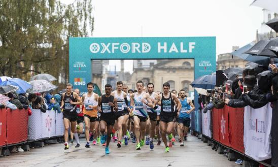 Image shows people running in the Oxford half marathon under an arch.