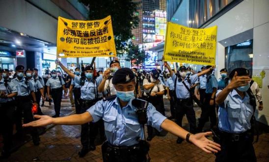 Hong Kong police in foreground shut down Tiananmen Square anniversary vigil - protesters hold placards in background