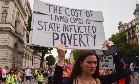 Woman at UK protest holds placards saying 'The Cost of Living Crisis is State Inflicted Poverty'