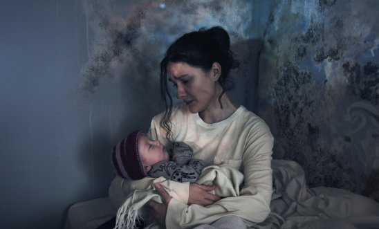 Woman holding baby in a room with moldy walls