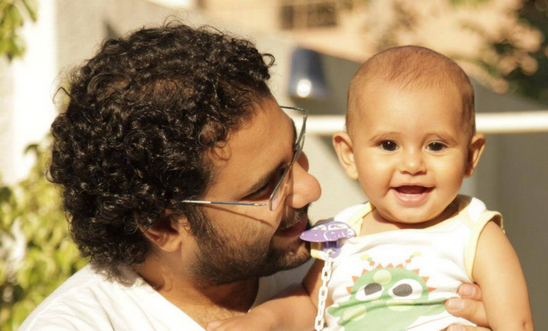 An image of Alaa Abd El Fattah cradling a beaming baby. (Image taken from another Amnesty post) An image of Alaa Abd El Fattah cradling a beaming baby. (Image taken from another Amnesty post)