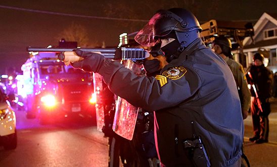 A police officer points a shotgun at protestors during a demonstration