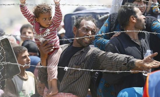 A Syrian refugee reacts as he waits behind border fences to cross into Turkey at A Syrian refugee reacts as he waits behind border fences to cross into Turkey at