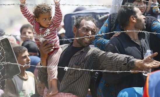 A Syrian refugee reacts as he waits behind border fences to cross into Turkey at