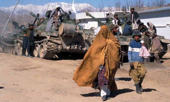 Afghan woman and boy walk by a tank in Kabul, 2004