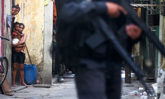 Residents look on as military police officers patrol in Complexo da Mare, favela