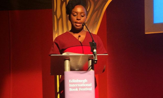 The picture shows an author standing at a podium speaking. The picture shows an author standing at a podium speaking.
