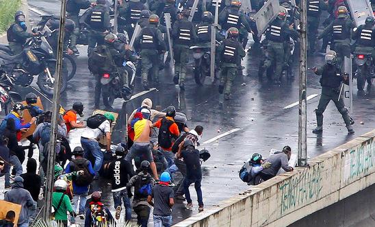 A member of the riot security forces points a gun towards a crowd of demonstrators in Venezuela A member of the riot security forces points a gun towards a crowd of demonstrators in Venezuela