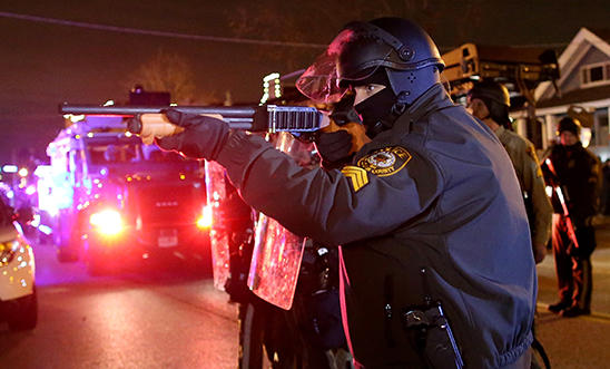 A police officer points a shotgun at protestors during a demonstration A police officer points a shotgun at protestors during a demonstration