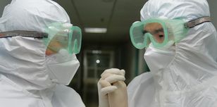 Two people in overalls, gloves and goggles, linking hands.