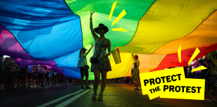 An image of a person under a rainbow flag while attending a protest for LGTBI+ rights