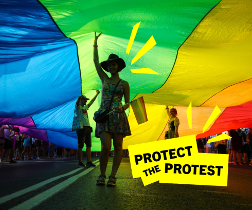 An image of a person under a rainbow flag while attending a protest for LGTBI+ rights